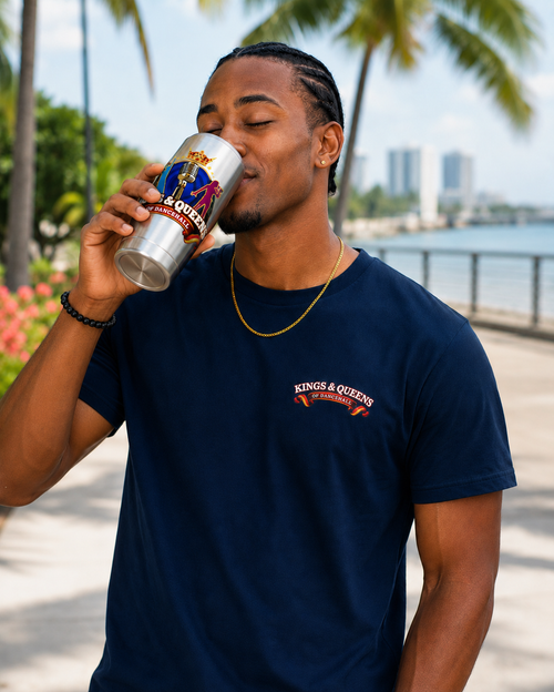 Man drinking from a Kings & Queens of Dancehall stainless tumbler on a palm-lined waterfront.